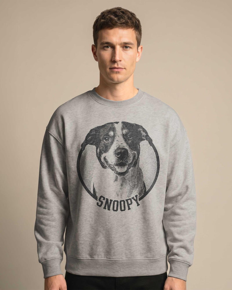 May include: A gray sweatshirt featuring a black and white dog portrait inside a circular frame. The word "SNOOPY" is printed in black below the dog image. The sweatshirt is a casual style.