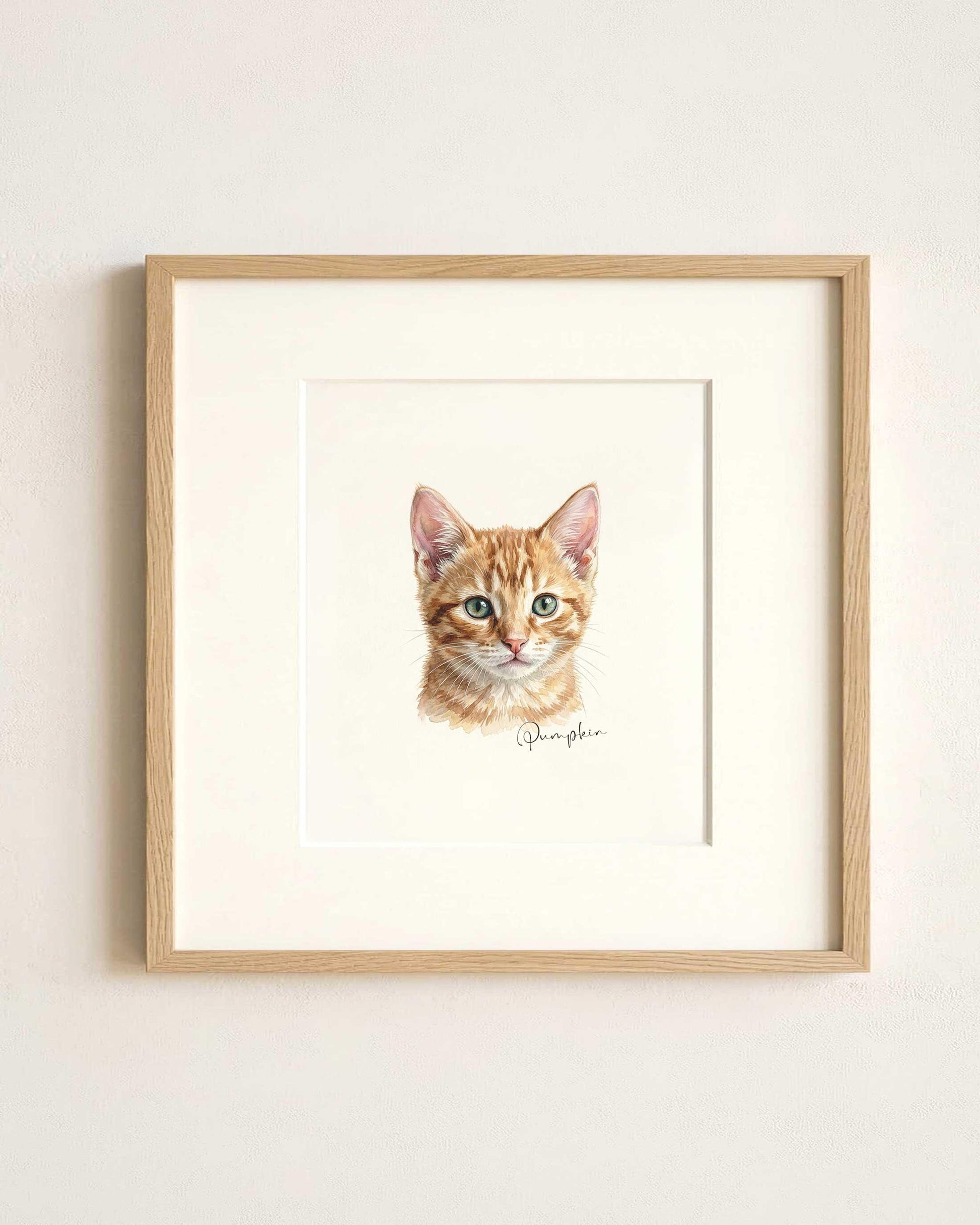 May include: A framed watercolor print of a ginger tabby kitten. The artwork features the kitten's head and shoulders, with detailed fur and green eyes. The print is set in a white mat and a light wood frame, with the name "Pumpkin" written in script.