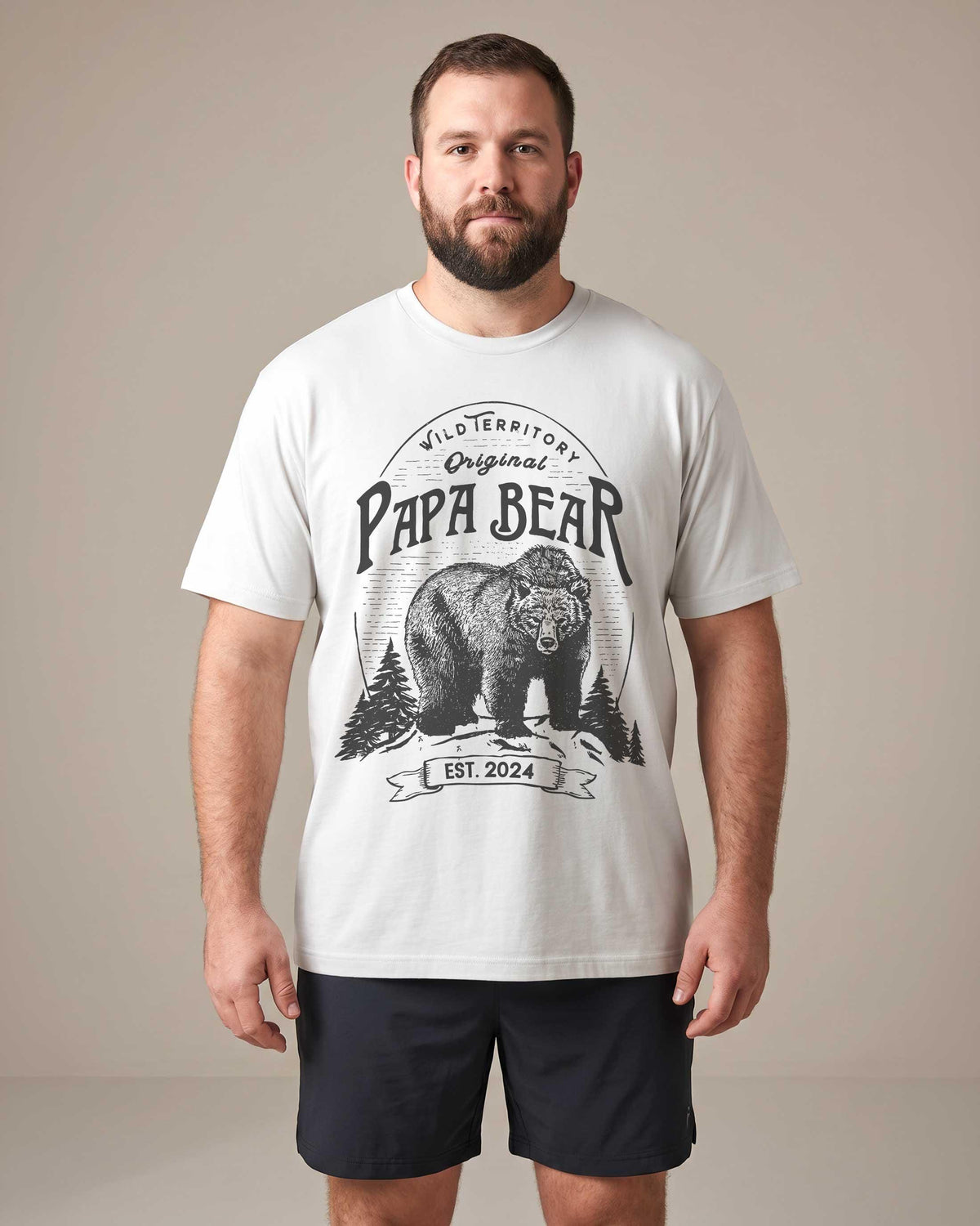 Bearded man wearing a white Papa Bear graphic t-shirt with a grizzly bear illustration and EST. 2024 printed below, surrounded by pine trees in a vintage badge design.